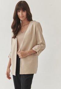 Beige neformální sako s ohrnutými rukávy, vyrobené z hladké látky, s klopovým límcem a dvěma předními kapsami, v kombinaci s béžovým topem.