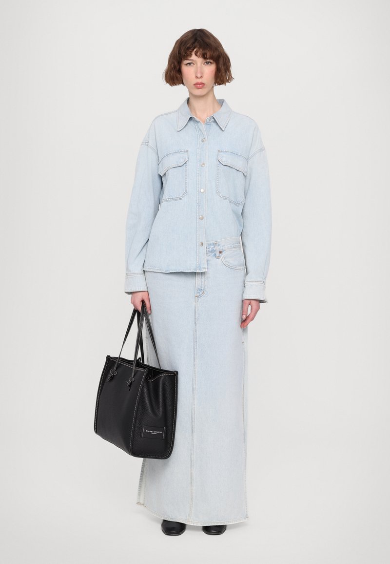 Giacca in denim azzurro chiaro con maniche lunghe, chiusura a bottoni e due tasche sul petto, abbinata a una lunga gonna in denim coordinata e una borsa a spalla nera.