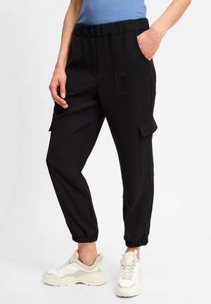 Black cargo pants with an elastic waistband, side pockets, and ankle cuffs; designed in a smooth, lightweight fabric. Paired with white sneakers.