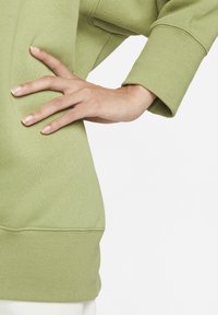 Ljusgrön sweatshirt med ribbade muddar och nederkant, med en avslappnad passform och mjuk textur. En märkbar detalj är sidoficköppningarna.