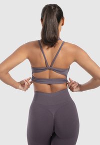 Paarse sportbeha met kruislings straps en uitsnijding aan de achterkant, gecombineerd met hoge, paarse leggings. Zachte, elastische stof.
