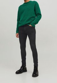 Suéter de punto verde con cuello redondo, tejido texturizado, combinado con jeans negros ajustados y botas negras con cordones.