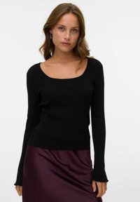 Haut à manches longues noir à côtes avec décolleté arrondi et coupe ajustée. Texture douce et manches évasées, associé à une jupe en satin violet profond.