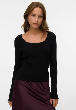 Haut à manches longues noir à côtes avec décolleté arrondi et coupe ajustée. Texture douce et manches évasées, associé à une jupe en satin violet profond.