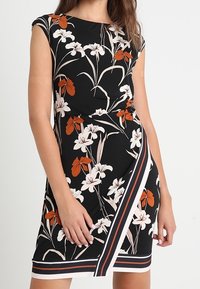 Vestido floral de tela negra, con patrones en blanco y naranja, mangas cortas, un diseño ajustado y un acento de dobladillo a rayas.