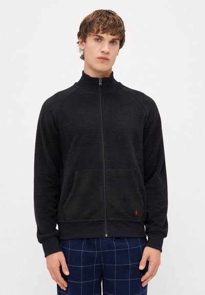 Schwarze Fleece-Zippjacke mit Stehkragen, Raglanärmel, zwei Fronttaschen und einem kleinen roten Logo auf der unteren linken Seite.