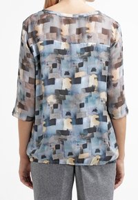 Blusa trasparente con un motivo rettangolare nelle tonalità di blu, grigio e beige. Maniche a tre quarti e una vestibilità morbida con scollatura rotonda.