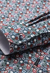 Buntes Hemd mit Knöpfen aus einem dunklen Stoff mit einem floralem Muster in Rot, Weiß und Grün, inklusive Knöpfen und einem Saumetikett.