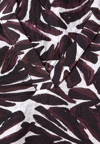 Blusa de escote en V con un audaz patrón de hojas abstractas en burdeos oscuro y blanco, confeccionada en una tela ligera y texturizada.
