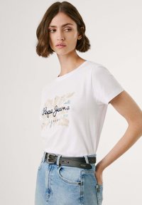 Vit T-shirt med kort ärm som har en flerfärgad grafisk design med texten "Pepe Jeans" och ett svart bälte med en silverdetalj på blå denim.