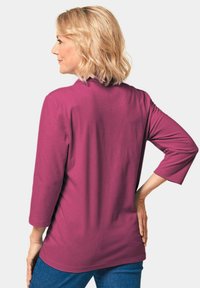 Fuchsia driekwart mouwtop van zachte stof, met een relaxte pasvorm en eenvoudige ronde halslijn. Gekocht met blauwe jeans.