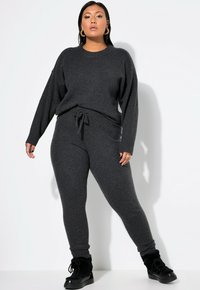 Dunkelgrauer Strickpullover mit Rundhalsausschnitt und überschnittenen Schultern, kombiniert mit passenden, enganliegenden Hosen und schwarzen Schnürstiefeln.