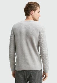 Grijze gebreide trui met een textuur op het lichaam en kabelbreipatroon op de mouwen. Ribboord aan de mouwen en onderkant maken het ontwerp af.