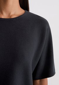 Zwarte gebreide t-shirt met een ronde halslijn en korte mouwen. De textuur lijkt zacht met een subtiel weefpatroon.