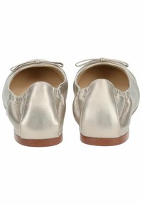 Bailarinas metálicas doradas con puntera redondeada, parte superior de cuero suave y un lazo decorativo en el talón. Suela plana de madera.