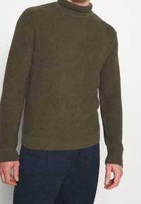 Olivgrön, ribbad turtleneck-tröja med en figursydd design och strukturerad stickning. Långa ärmar, enfärgad och rak nederkant.