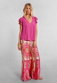 Top rosa a V con maniche a volant abbinato a pantaloni larghi a fantasia con un design paisley rosa e oro. Texture liscia.