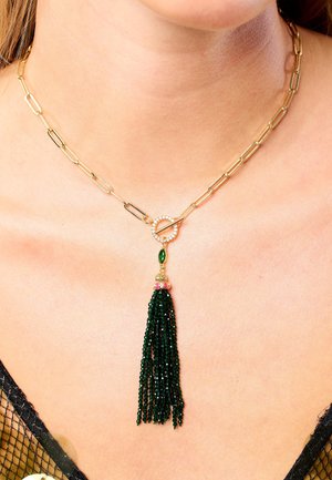 Collier en chaîne dorée avec des maillons en forme de trombone, un fermoir rond orné de pierres transparentes et un pendentif à frange en perles vertes.