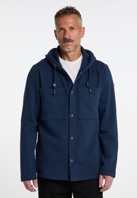 Veste à capuche bleu marine en tissu texturé, dotée de deux poches avant, d'une fermeture à bouton et de cordons de serrage réglables sur la capuche.