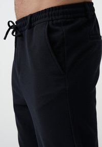 Schwarze, strukturierte Jogginghosen mit einem elastischen Bund und Kordelzug, ausgestattet mit Seitentaschen und einem schlanken Schnitt.