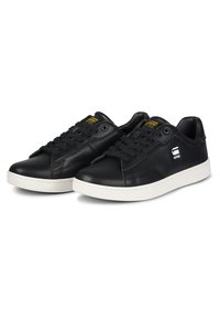 Black leather sneakers with a white rubber sole, round toe, and lace-up design. Features stitched accents and a logo detail on the side.