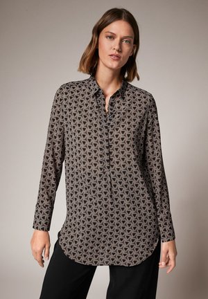 Zwarte langemouwen shirt met een geometrisch patroon. Voorzien van een knoopsluiting kraag en een afgeronde zoom, gemaakt van een gladde stof.