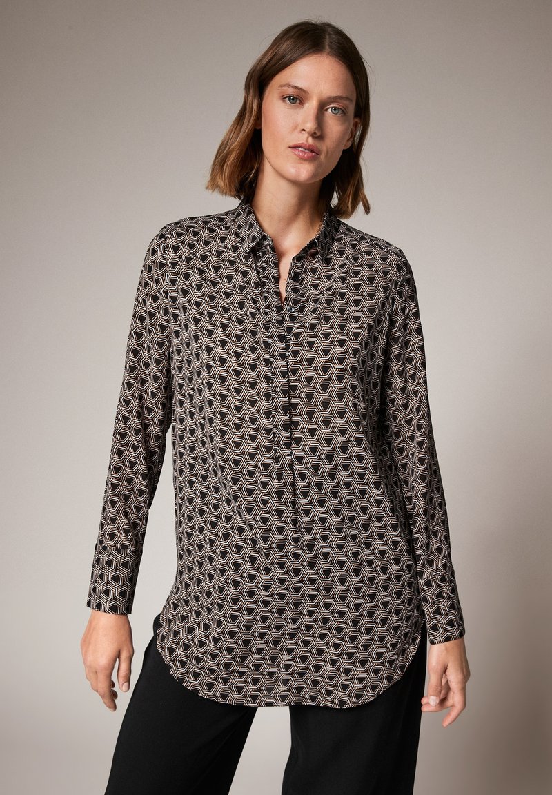 Zwarte langemouwen shirt met een geometrisch patroon. Voorzien van een knoopsluiting kraag en een afgeronde zoom, gemaakt van een gladde stof.