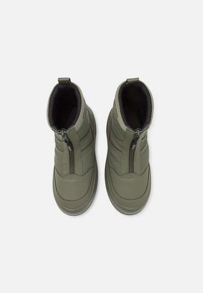 Des bottes vertes résistantes à l'eau présentent une tige haute, une fermeture éclair, un intérieur rembourré et des détails texturés sur les côtés et le dessus.