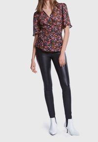 Schwarzes, blumengemustertes Wickeloberteil mit kurzen Ärmeln, kombiniert mit schwarzen leggingsähnlichen Leggings und weißen Knöchelstiefeln. Das Outfit hat eine taillierte Silhouette.