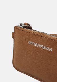 Brun læder lynlåspung med sølv hardware og præget "Emporio Armani" logo. Har en glat tekstur og et rent, klassisk design.