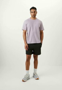 T-shirt lilás de manga curta com decote redondo e costura tonal, combinado com calções pretos e sapatilhas desportivas cinzentas claras com pormenores em laranja.
