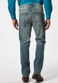 Vaqueros de mezclilla azul claro con corte recto, cinco bolsillos y un ligero desgastado. Combinados con zapatos de vestir marrones y una camisa de botones turquesa.