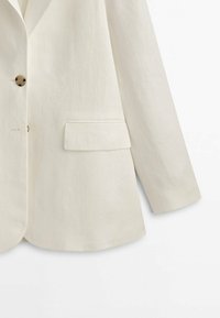 Blazer beige à simple boutonnage avec boutons en écaille, poche à rabat sur le côté droit et manches longues.