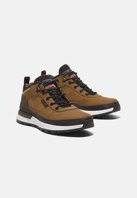 Zapatos de senderismo de cuero marrón y textil con acentos en negro, cuello acolchado, suela media gruesa blanca y cordones contrastantes. Presenta un logo en el panel lateral.