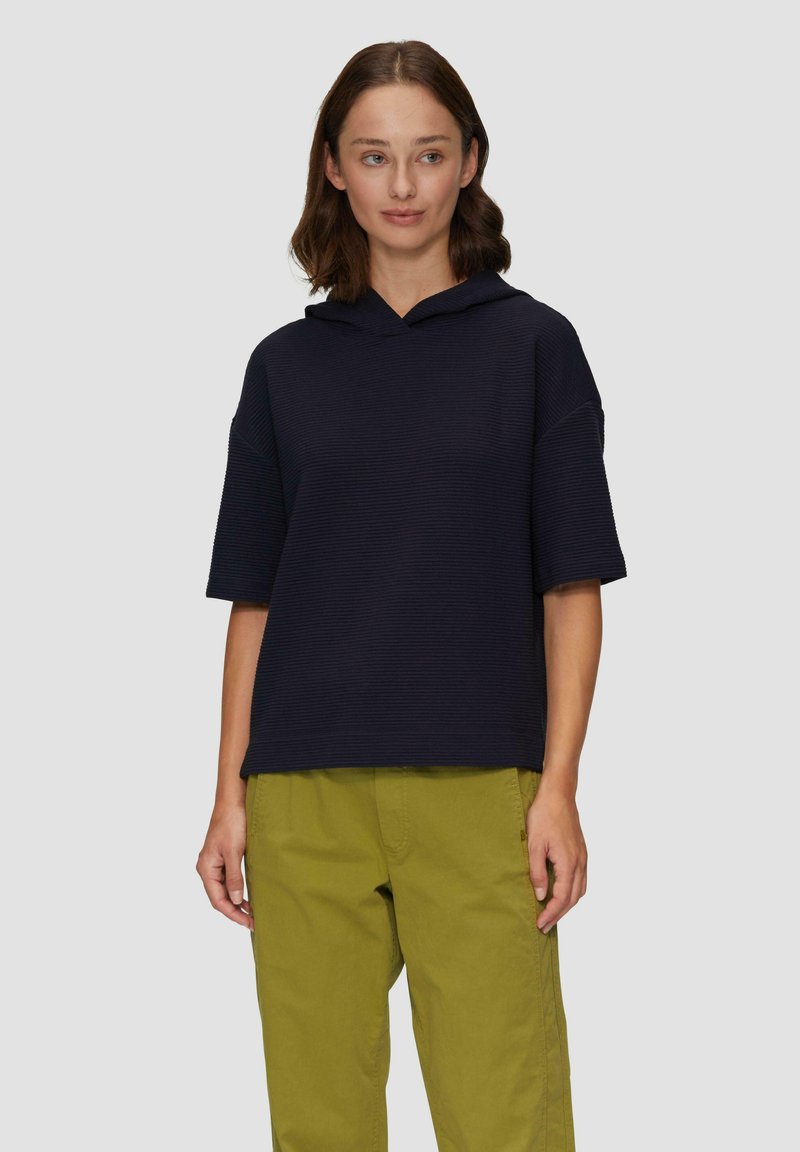 Granatowy fason z kapturem, o teksturowanym, prążkowanym wzorze i krótkich rękawach, w połączeniu z jasnoskalnym zielonymi spodniami. Prosty, luźny kształt.