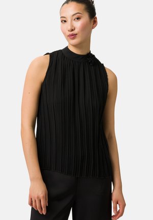 Blusa nera plissettata senza maniche con colletto alto e dettaglio floreale al collo. Tessuto liscio, che mette in risalto pieghe verticali, abbinata a pantaloni neri.