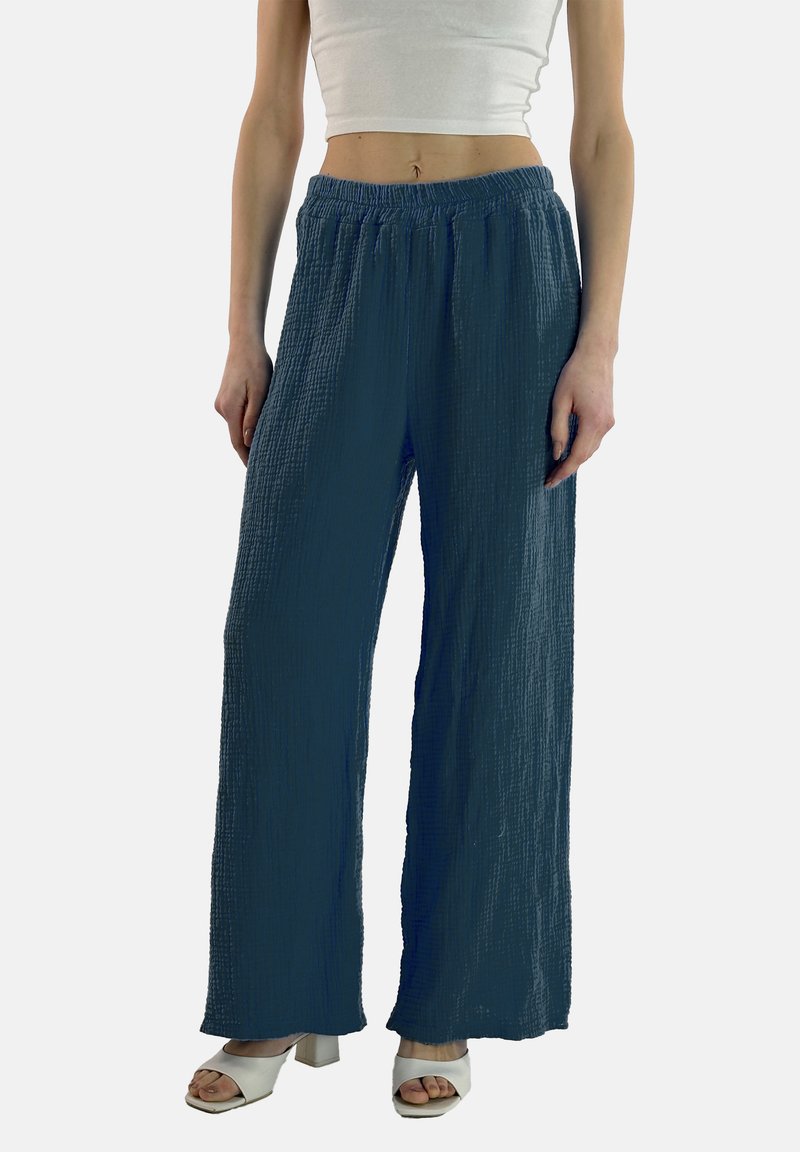 Lange, getextureerde broek in donkerblauwe stof met een elastische tailleband, gecombineerd met witte sandalen met een dikke hak.