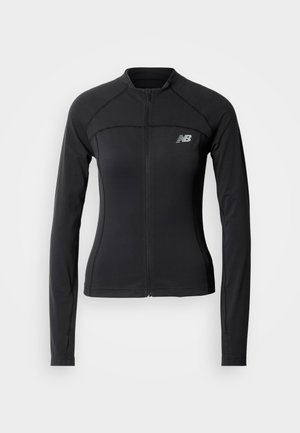 Sort atletisk jakke med glidelås foran, lange ermer, buede sømdetaljer og en reflekterende logo på venstre bryst. Jevn stofftekstur.