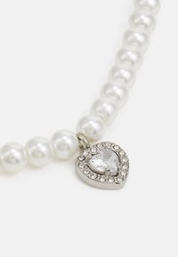 Collana di perle con perle bianche rotonde e lucide, accompagnata da un pendente a forma di cuore in argento con una pietra trasparente circondata da piccole paillettes.