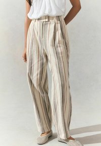 Pantalons crème rayés avec des lignes verticales rouges, vertes et noires. Présentent une taille haute et des plis, fabriqués en tissu léger.