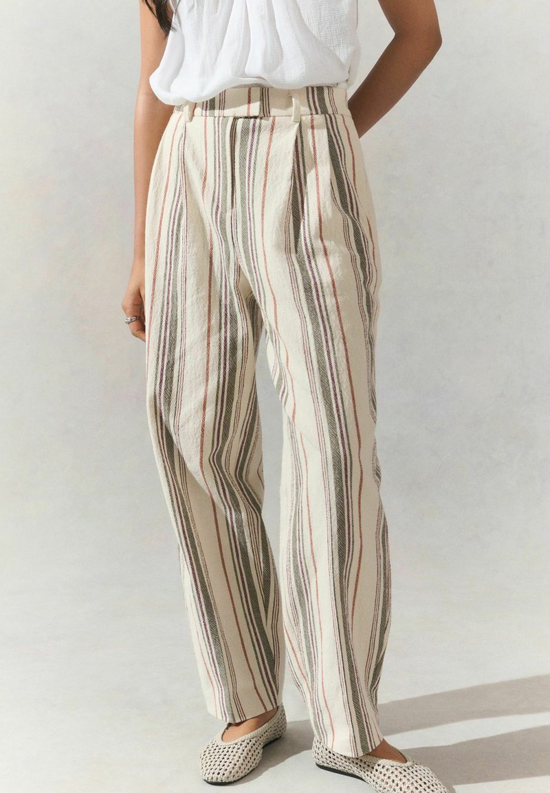 Pantalons crème rayés avec des lignes verticales rouges, vertes et noires. Présentent une taille haute et des plis, fabriqués en tissu léger.