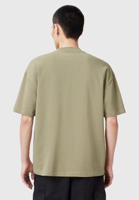 T-shirt khaki a maniche corte con fitting rilassato, scollatura a girocollo e cuciture in evidenza. Materiale in cotone morbido con una texture liscia.