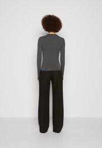 Långärmad grå topp med en figursydd design, kombinerad med högmidjade svarta byxor. Slät textur, enkel halsringning och skräddarsydd siluett.