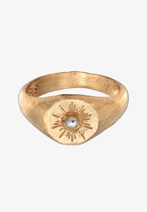 Goldener Siegelring mit Sonnenstrahlmuster und einem zentralen weißen, perlenähnlichen Stein auf einfachem weißen Hintergrund.