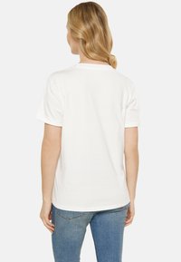 Hvid bomulds T-shirt med rund hals, korte ærmer og opkrøllede manchetter. Blød tekstur med en lige snit og en lidt længere bagsøm.
