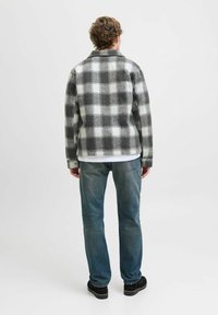 Sort-hvid ternet flanneljakke med krave, vist fra ryggen, parret med lyseblå jeans og sorte sko.