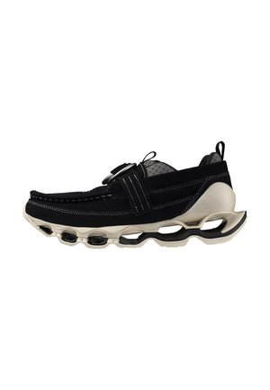 Sneaker nera con suola beige spessa con ammortizzazione ad aria aperta, cinturino nero con fibbia argentata e linguette sul tallone e sulla lingua.