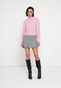 Ανοιχτό ροζ πουλόβερ πλεκτό με ζιγκ-ζαγκ μοτίβο, σε συνδυασμό με γκρι μίνι φούστα με πιέτες. Το μοντέλο φοράει μαύρες μπότες μέχρι το γόνατο και μοβ γυαλιά ηλίου.