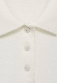 Witte zachte stoffen kraag van een shirt met drie witte knopen die aan de voorkant zijn vastgemaakt.
