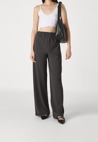 Pantalones negros de pierna ancha con una cinturilla elástica, combinados con una camiseta corta blanca. La modelo lleva un bolso negro de hombro y calza planos puntiagudos.